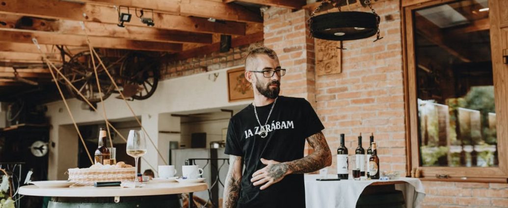 Man in rustic winery setting with bottles and wooden barrels, embracing a casual vibe.